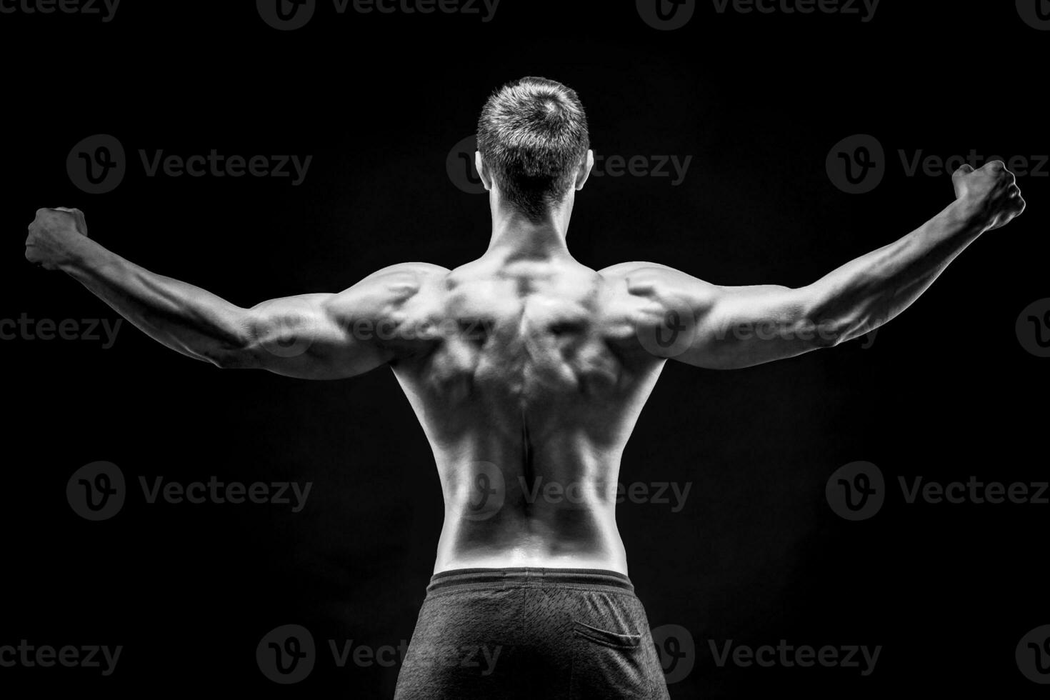 Rear view of muscular young man showing back, biceps muscles photo