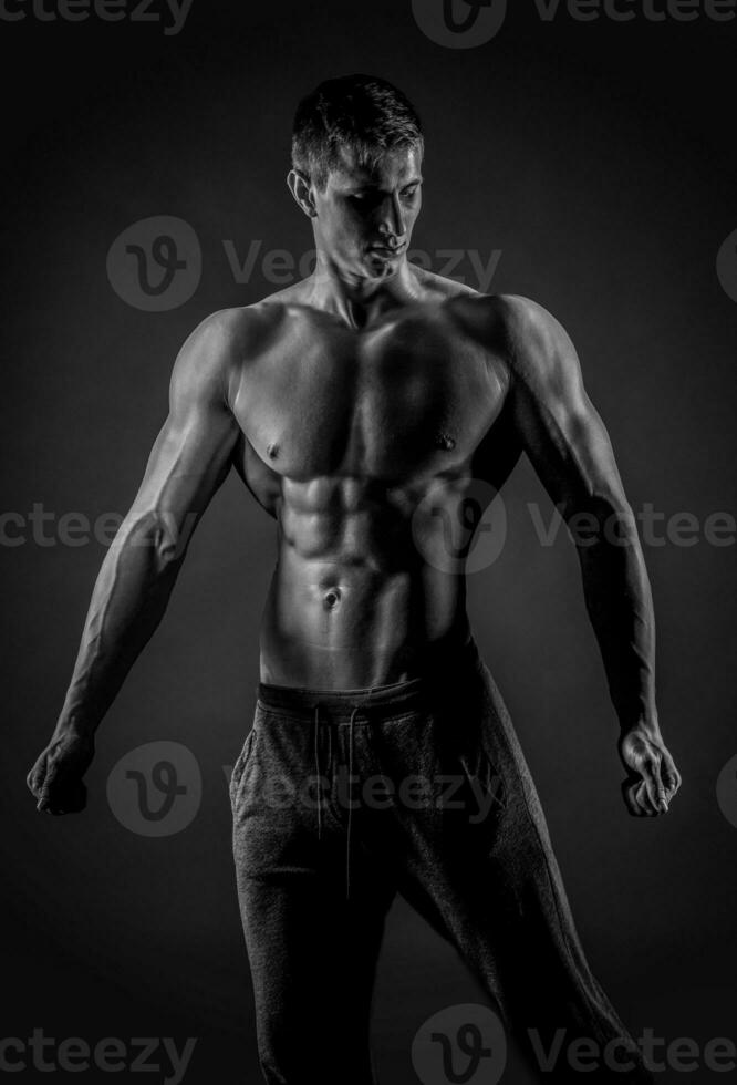 Sexy muscular man posing with naked torso on black background photo