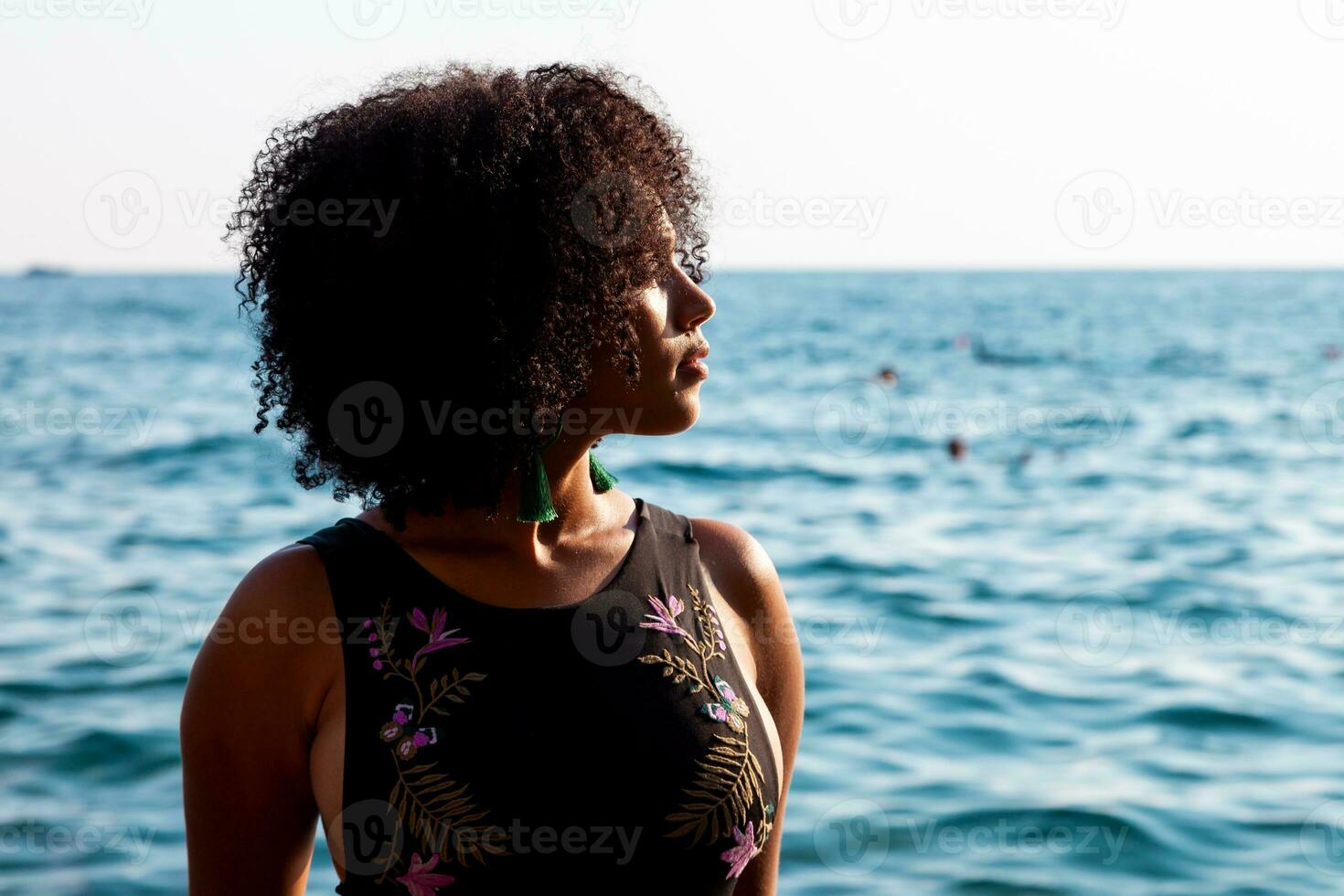 retrato de un bonito Rizado venezolano mujer relajante en un rock en el mar foto