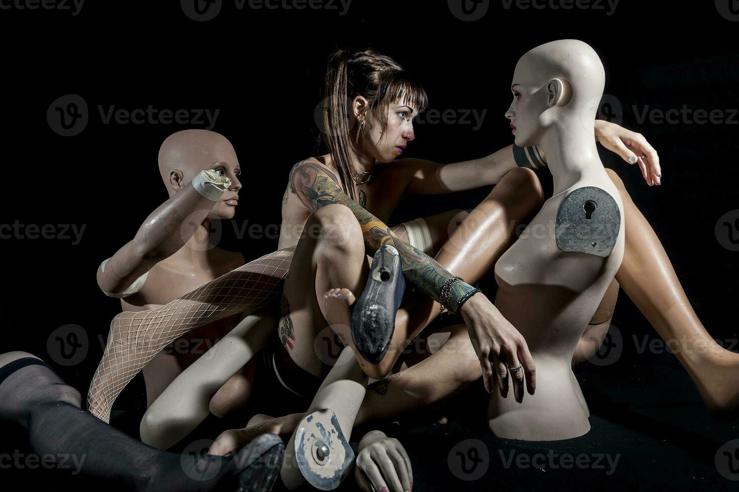 young tattooed woman while hugging two naked and broken mannequins photo