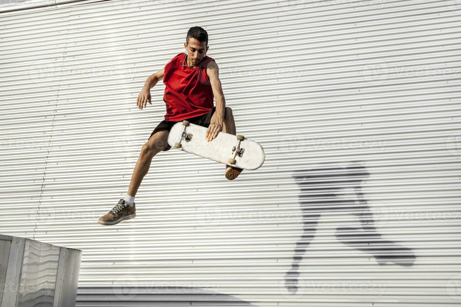 joven skater saltos arriba con su tablero en frente de un metal antecedentes foto