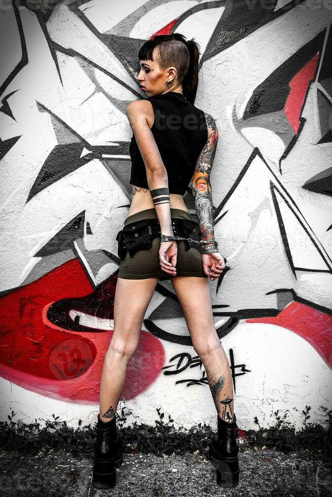 rebelde niña tatuado en contra un pintado pared con pintada foto
