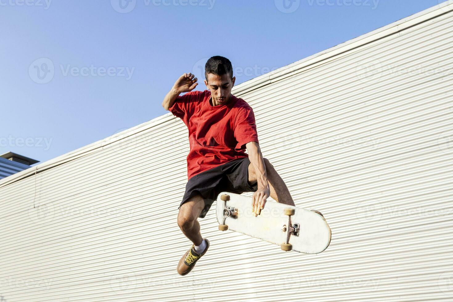 young skateboarder jumps up with his board in front of a metal background photo