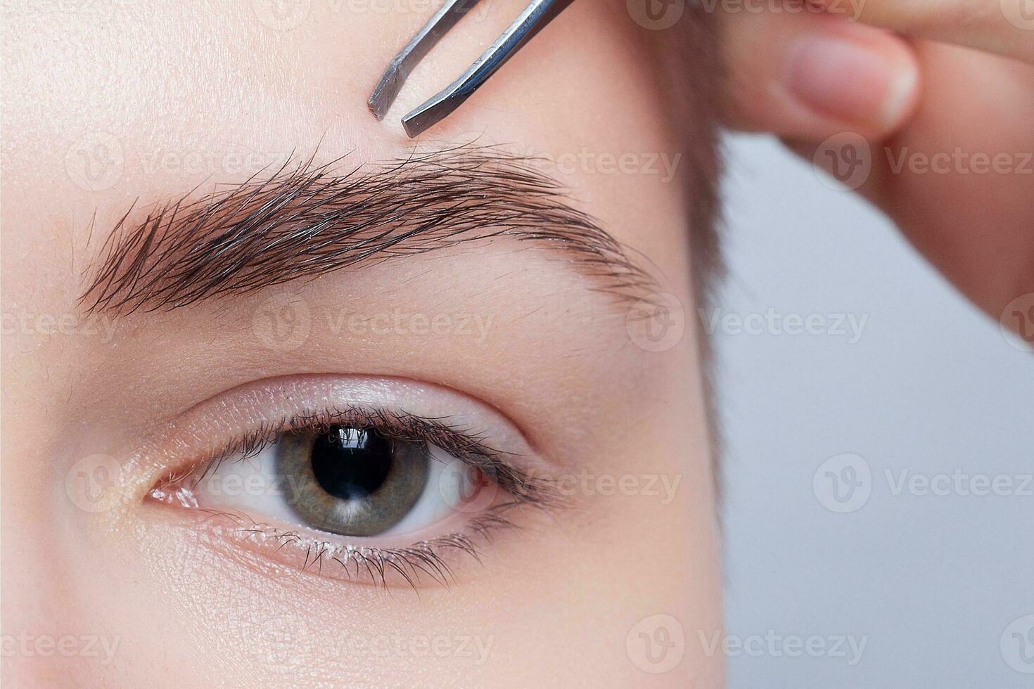 Young woman with short hair plucking eyebrows tweezers close up photo