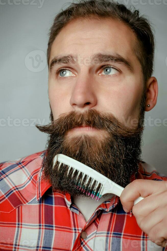young man comb his beard and moustache  gray background photo