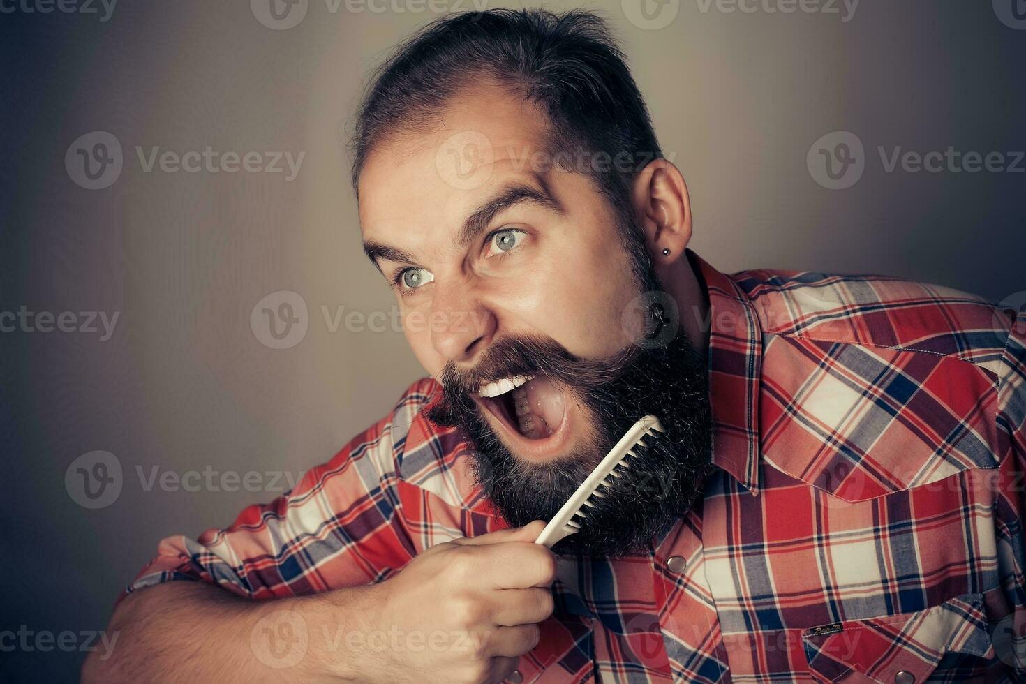 young man comb his beard and moustache on gray background photo