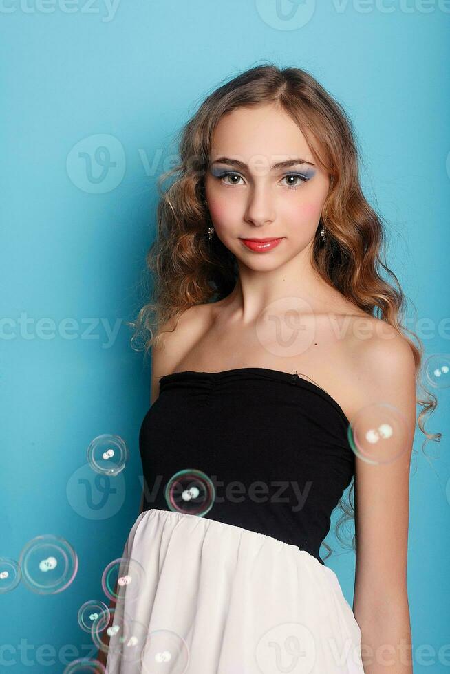 Beautiful young woman with soap bubbles over cyan background photo