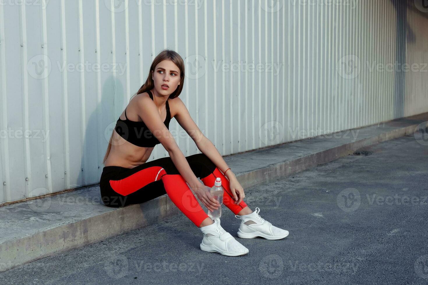 hembra atleta Bebiendo agua mientras en pie por un gris pared. foto
