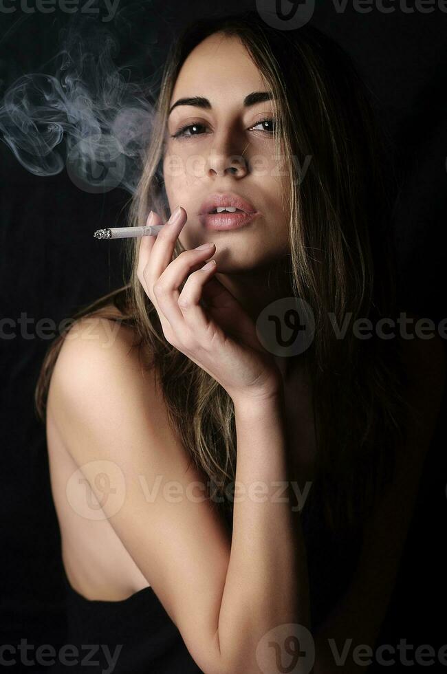 elegante mujer morena fumando un cigarrillo con fondo negro foto