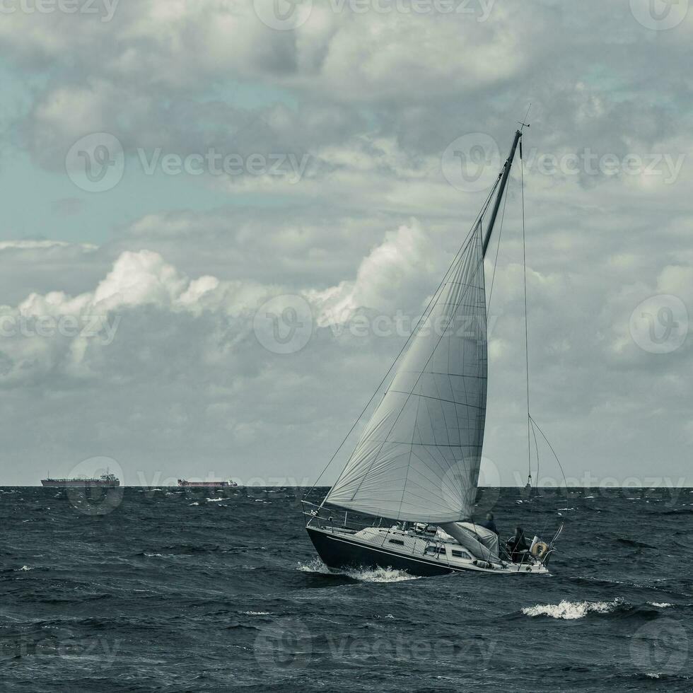 Blue sailboat in a travel at stormy sea. Regata journey. Toned photo
