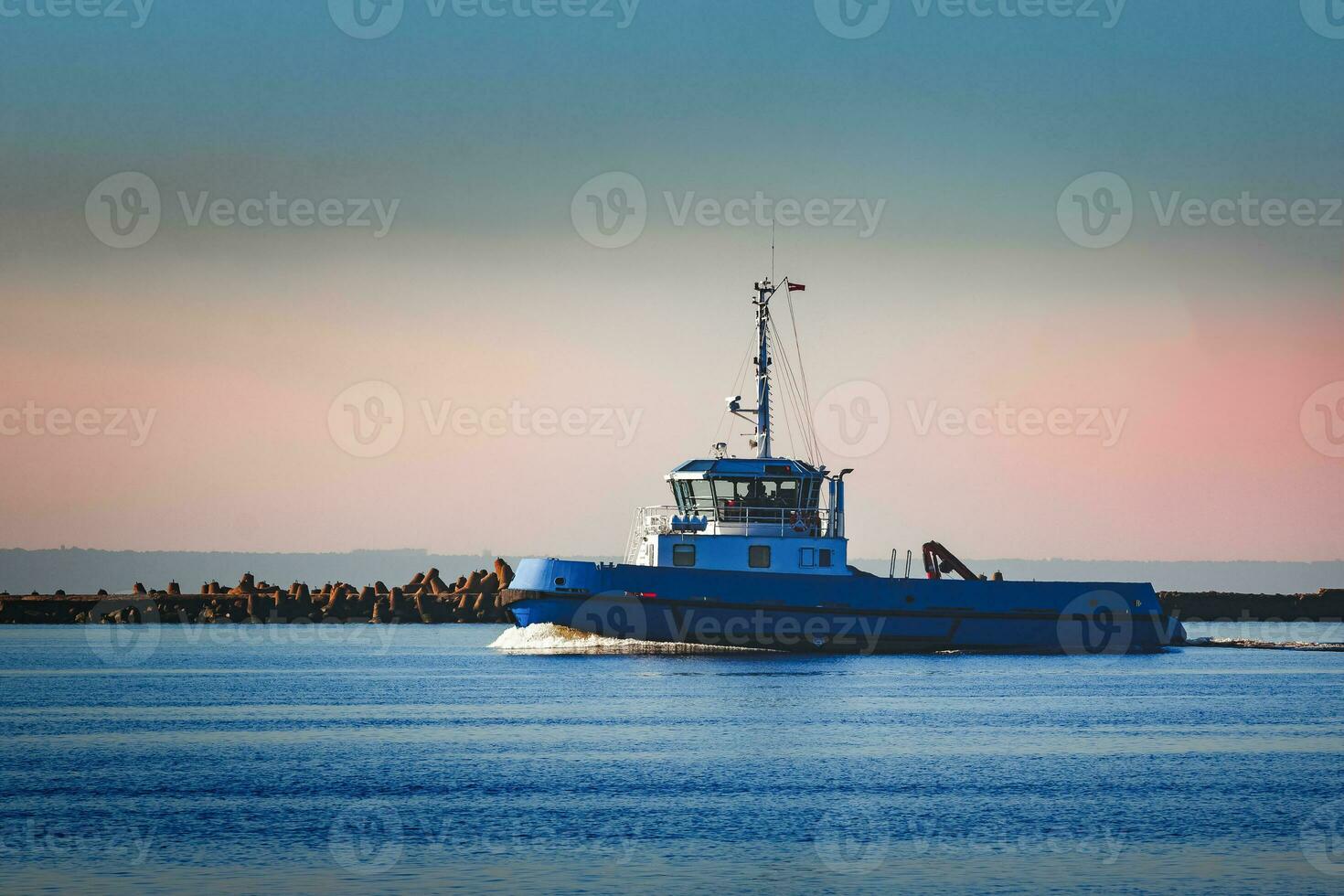 Blue small tug ship sailing past the breakwater dam in morning photo