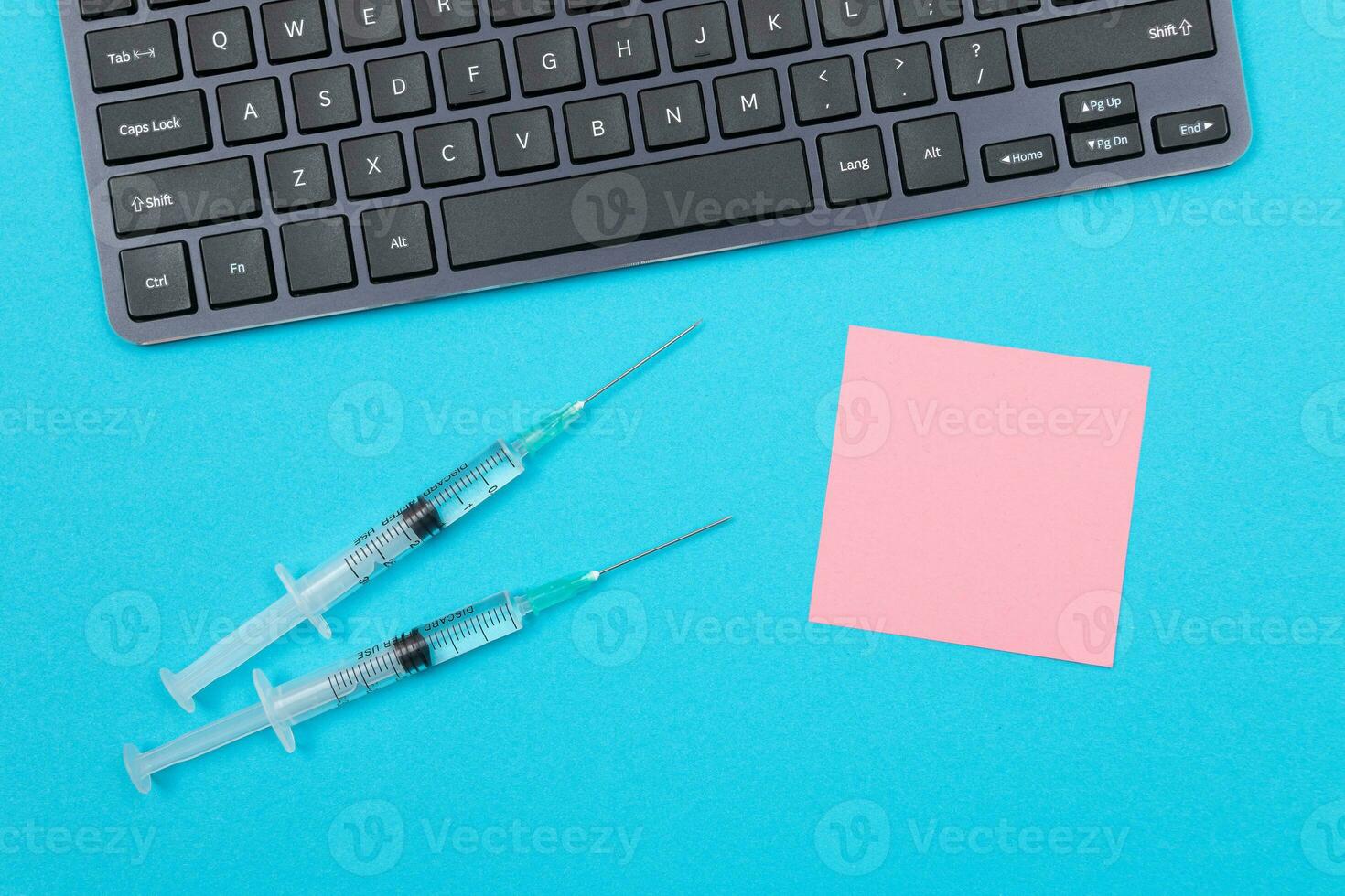 Vaccination, Immunology or Revaccination Concept Two Medical Disposable Syringe Lying on Blue Table in Doctor's Office in a Hospital or Clinic. Blank Pink Sticky Note Mock Up with Copy Space photo