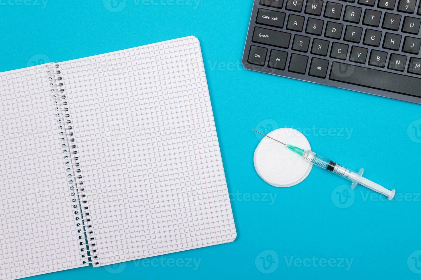 Vaccination, Immunology or Revaccination Concept A Medical Syringe Lying on Blue Table in Doctor's Office in a Hospital or Clinic. Opened Blank Notepad Mock Up with Copy Space photo