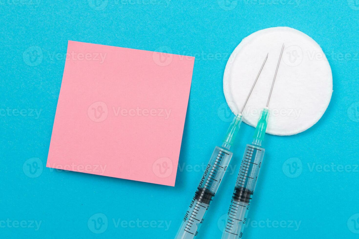 Vaccination, Immunology or Revaccination Concept Two Medical Disposable Syringe Lying on Blue Table in Doctor's Office in a Hospital or Clinic. Blank Pink Sticky Note Mock Up with Copy Space photo