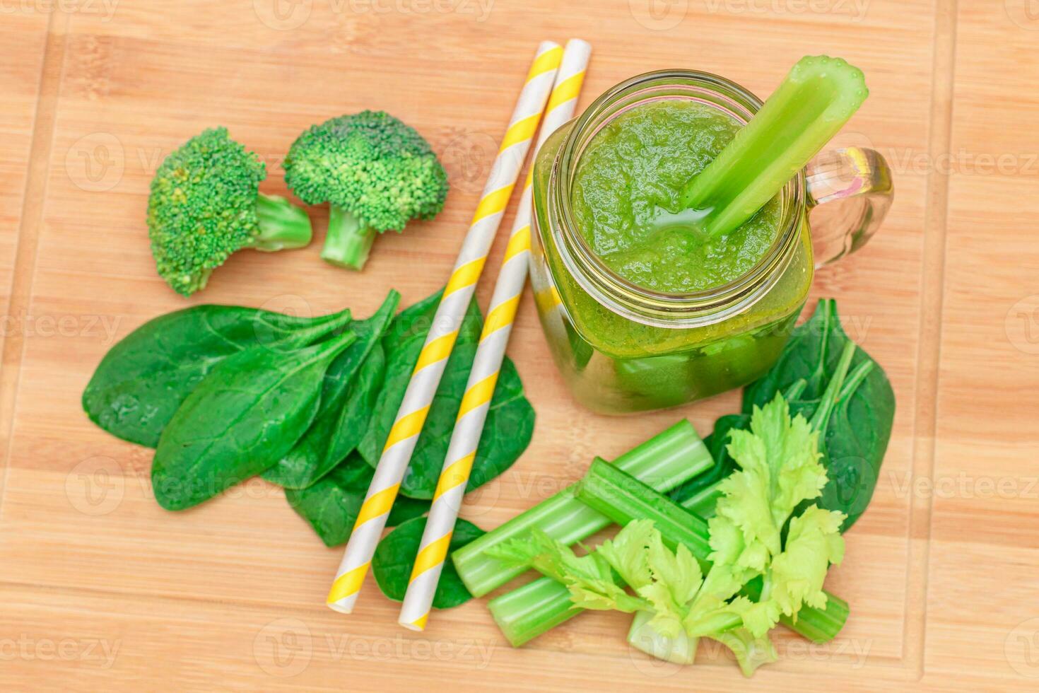 Fresh Green Smoothie of Apple, Celery, and Spinach in Glass Smoothie Jar with Yellow Cocktail Straw on Wooden Cutting Board. Vegan Detox Drink. Vegetarian Culture. Healthy Eating and Fruit Diet photo