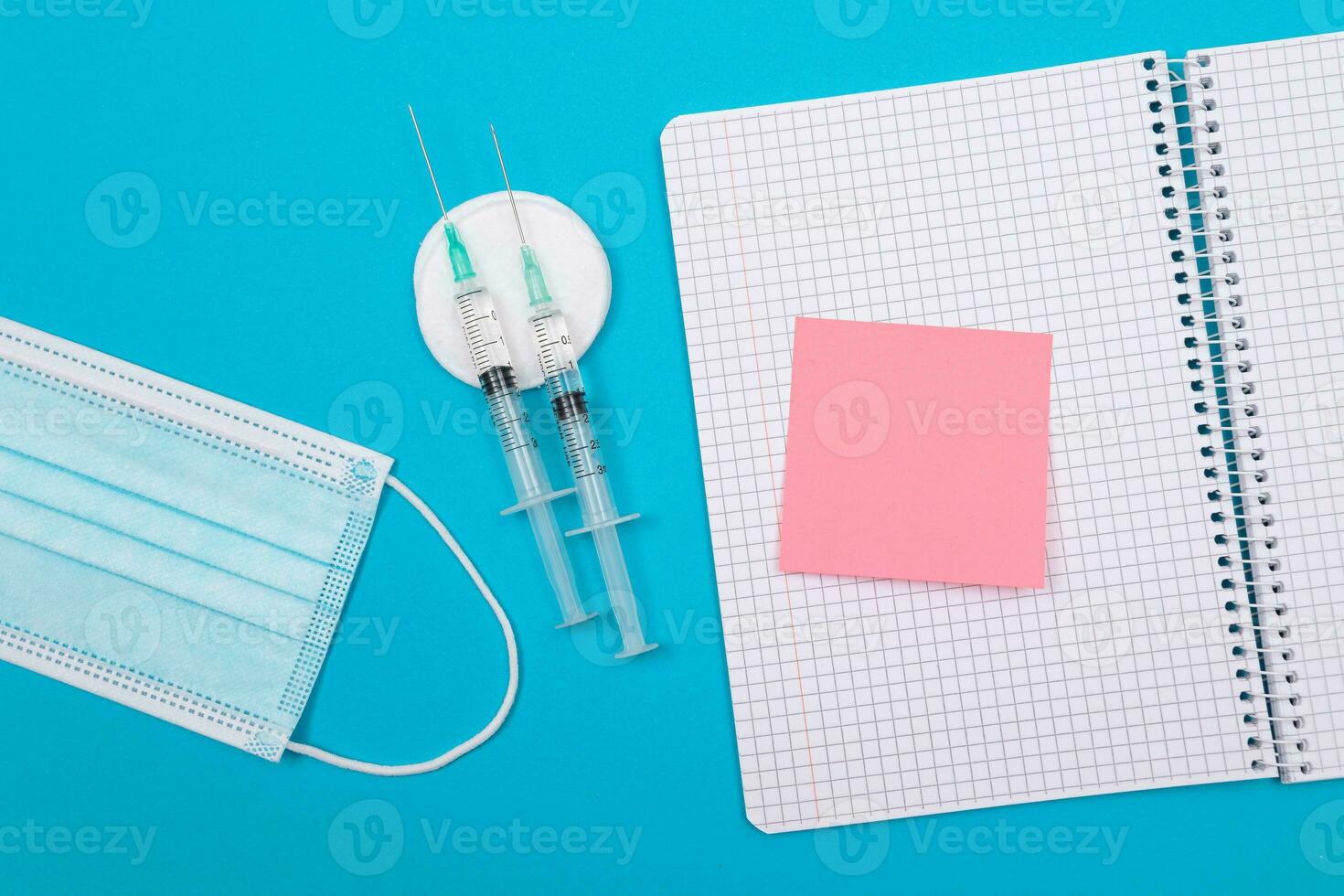 Vaccination, Immunology or Revaccination Concept Two Medical Disposable Syringe Lying on Blue Table in Doctor's Office in a Hospital or Clinic. Blank Pink Sticky Note Mock Up with Copy Space photo