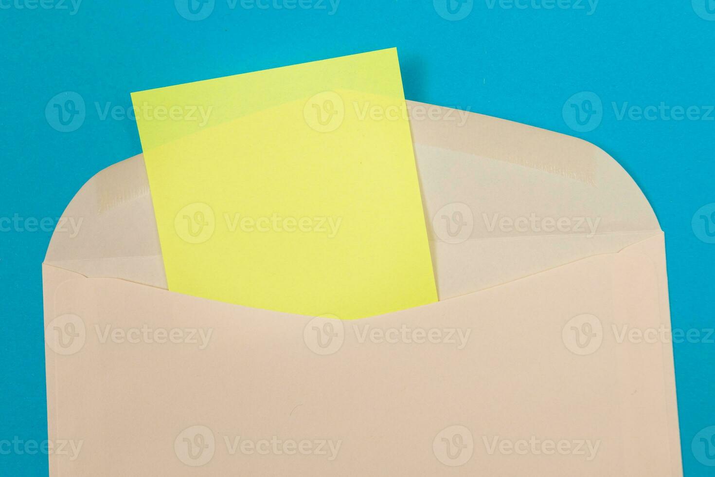 Beige Envelope with Blank Yellow Sheet of Paper Inside, Lying on Blue Background Mock Up with Copy Space. Receiving Mail or Notice, Sending Postcard Top View, Flat Lay photo