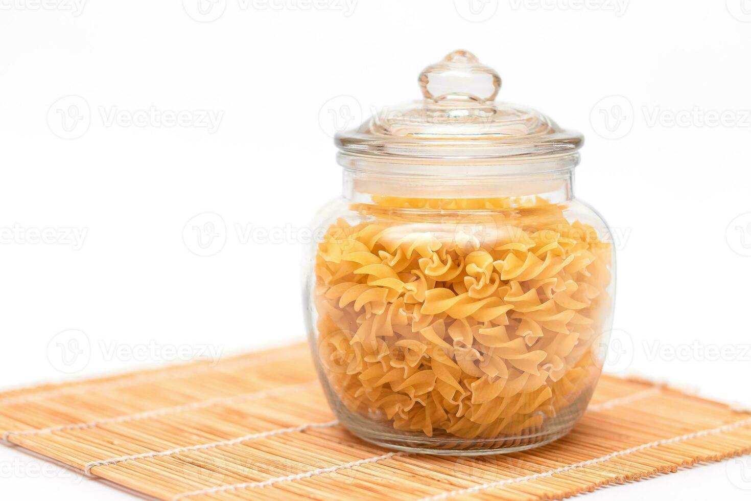 sin cocer fusilli pasta en vaso tarro en blanco antecedentes. crudo y seco macarrones. insalubre y grasa alimento. italiano cultura foto