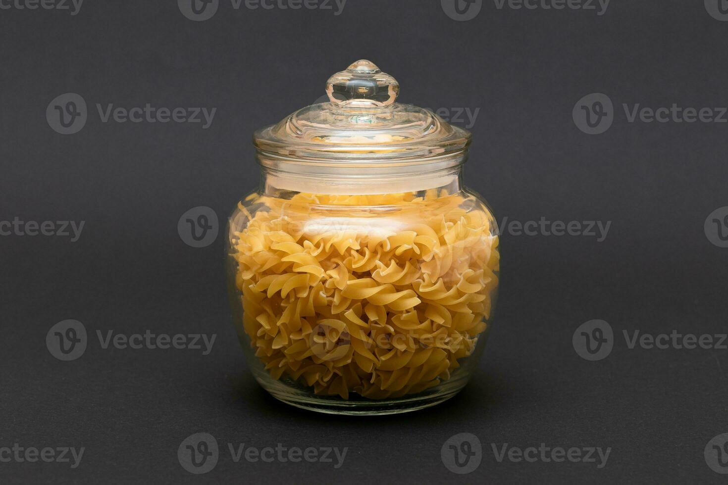 Uncooked Fusilli Pasta in Glass Jar on Black Background. Raw and Dry Macaroni. Unhealthy and Fat Food. Italian Culture photo