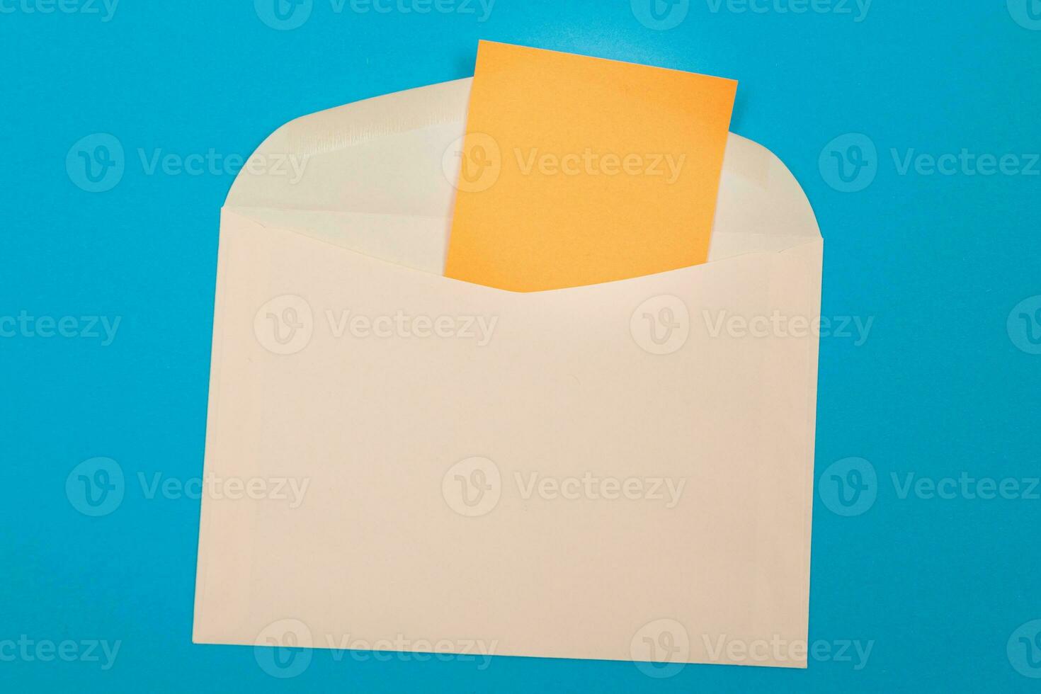 Beige Envelope with Blank Orange Sheet of Paper Inside, Lying on Blue Background Mock Up with Copy Space. Receiving Mail or Notice, Sending Postcard Top View, Flat Lay photo