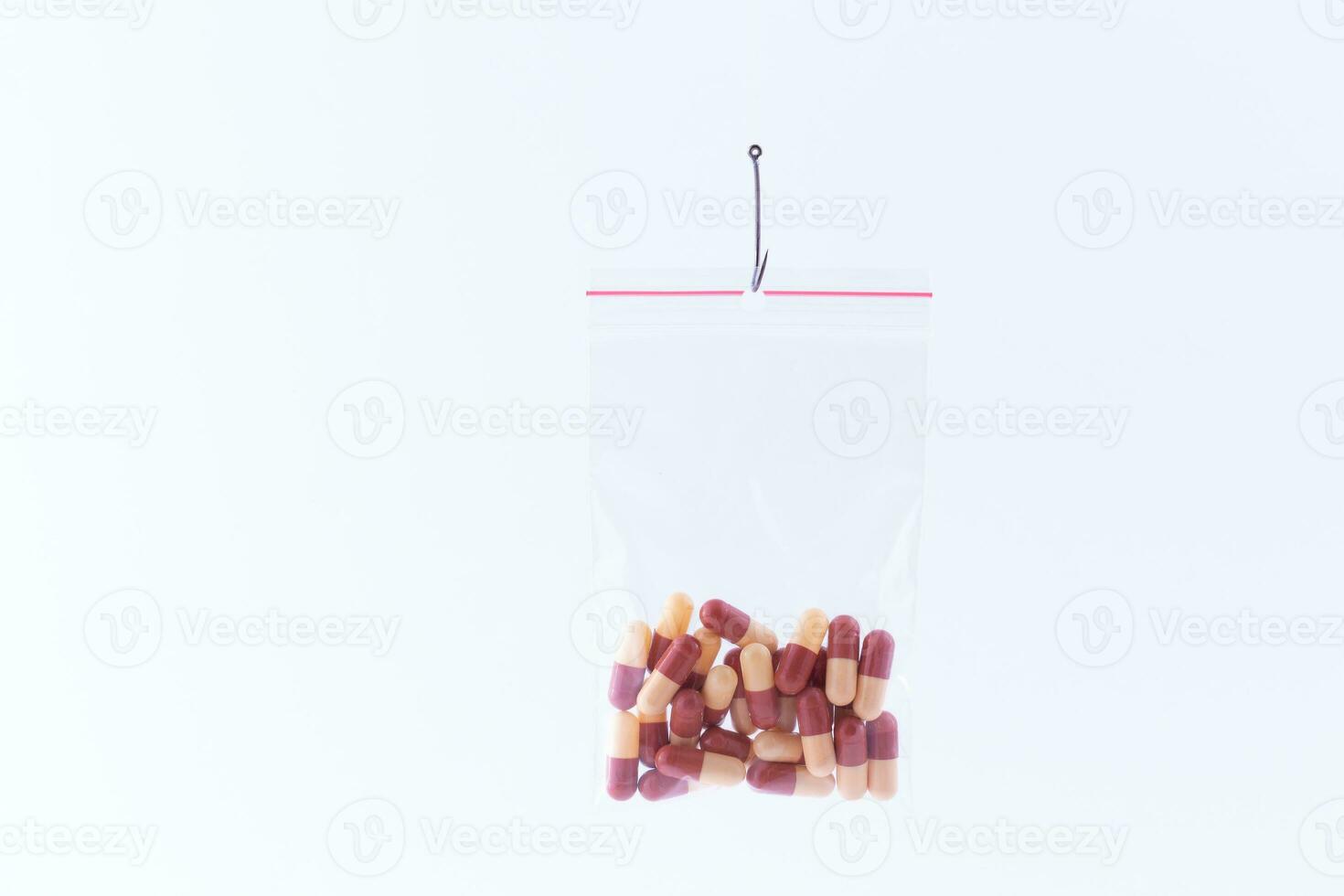 The Pharmaceutical Trap and Drug Addiction Colored Pills or Tablets Hanging in Small Ziplock Bag on a Fishing Hook Against the White Background photo