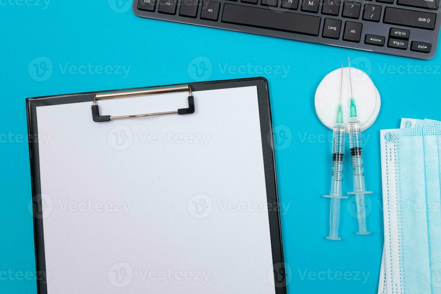 Vaccination, Immunology or Revaccination Concept Two Medical Syringe Lying on Blue Table in Doctor's Office in a Hospital or Clinic. Black Clipboard with Sheet of Paper Mock Up with Copy Space photo