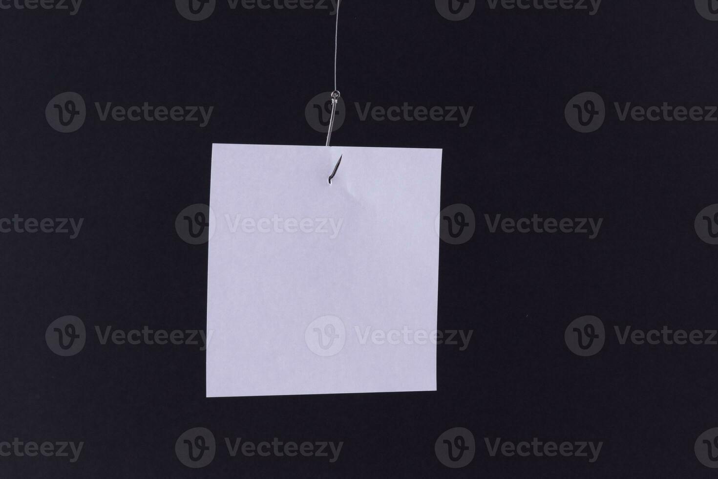 Mockup of a Blank White Memo Paper with Copy Space Hanging on a Fishing Hook Against the Black Background. Reminder or To Do List. Sticky Note Template photo