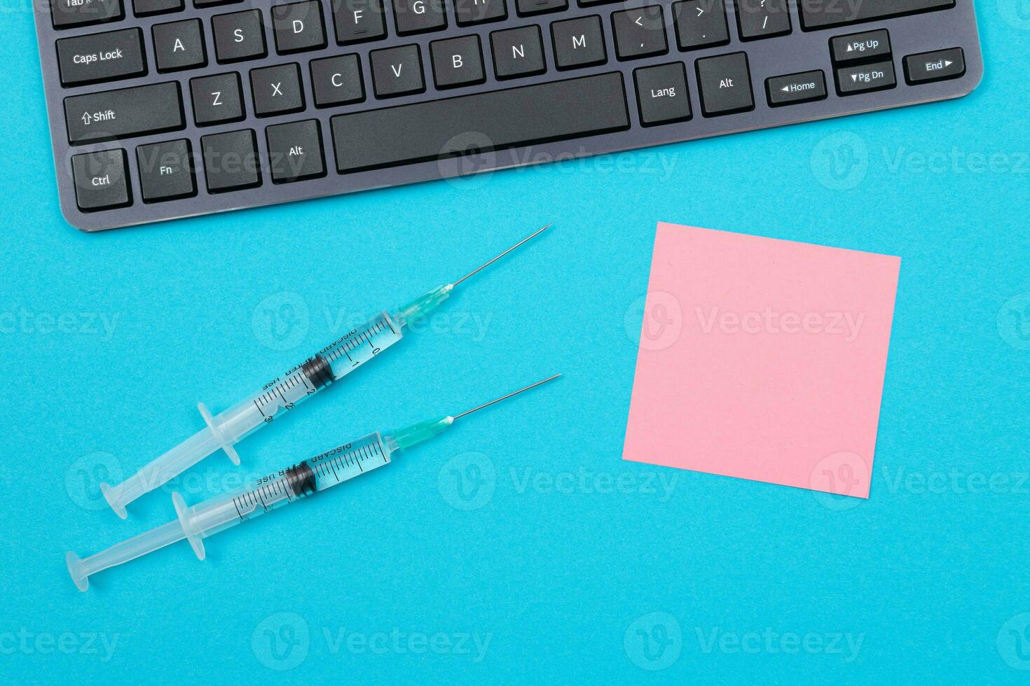 Vaccination, Immunology or Revaccination Concept Two Medical Disposable Syringe Lying on Blue Table in Doctor's Office in a Hospital or Clinic. Blank Pink Sticky Note Mock Up with Copy Space photo