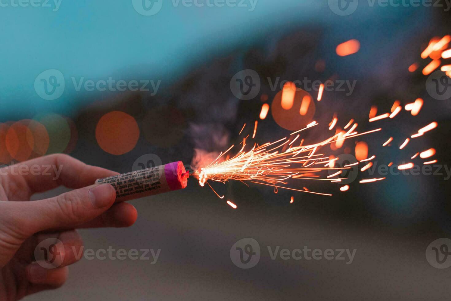 Young Man Lighting Up Firecracker in his Hand Outdoors in Evening. Guy Getting Ready for New Year Fun with Fireworks or Pyrotechnic Products CloseUp Shot photo