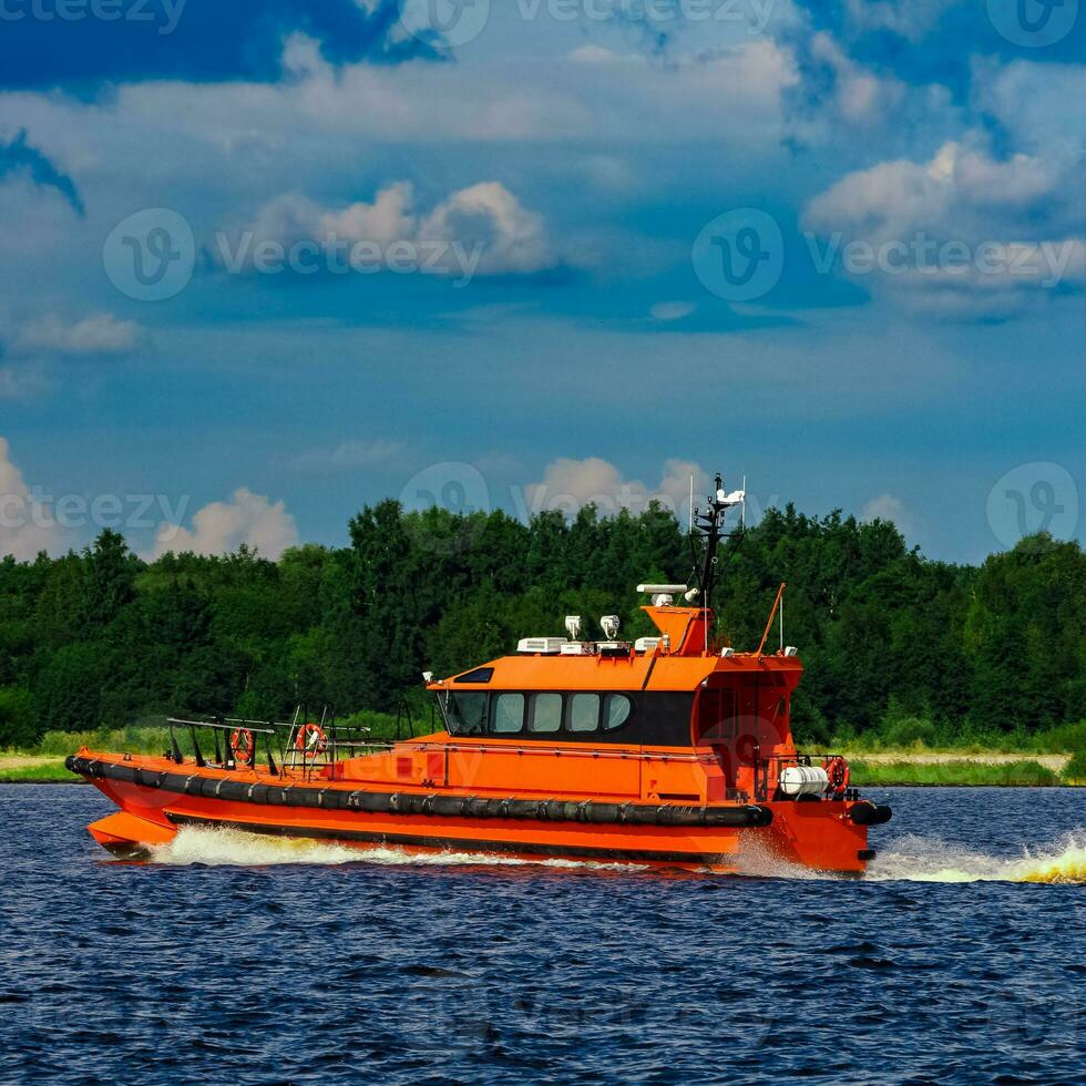 Orange pilot boat moving by the river in Europe. Rescue service photo