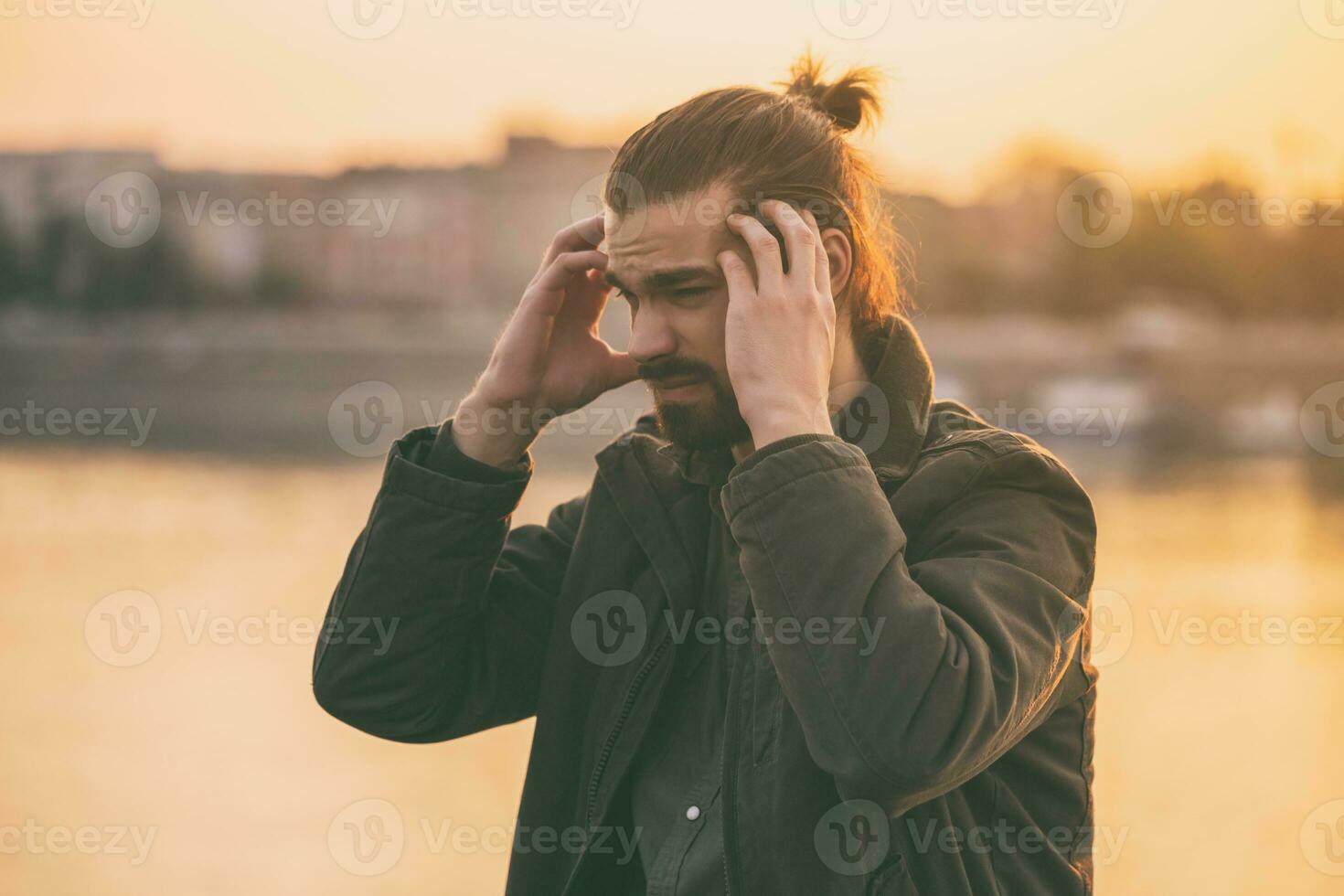 Young modern businessman is having a headache while sitting by the river.Toned image photo