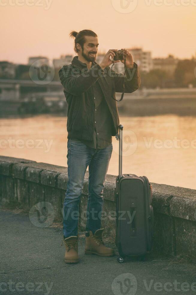 Handsome modern businessman with suitcase enjoys photographing city.Toned image photo