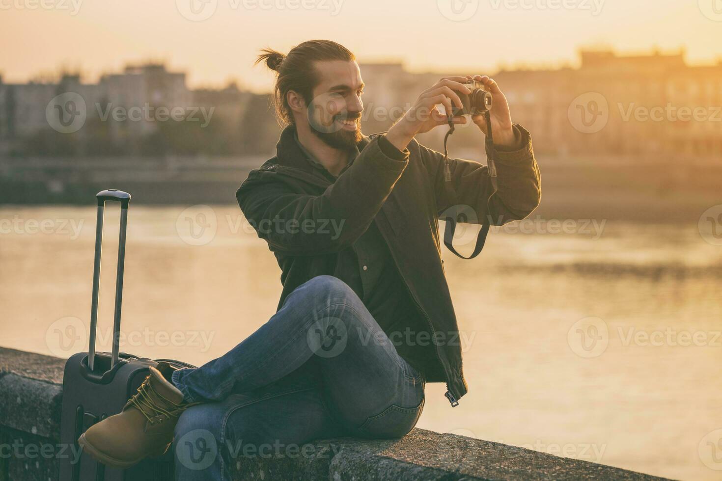 Handsome modern businessman with suitcase enjoys photographing city.Toned image photo