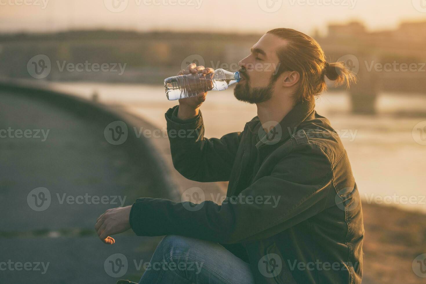 Handsome modern businessman enjoys drinking water and resting by the river.Toned image photo