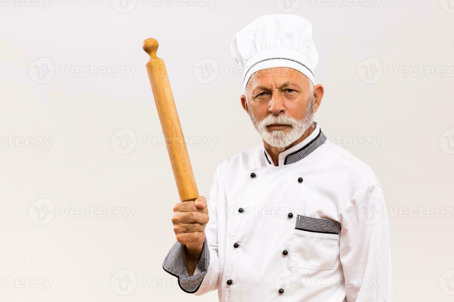 Image of angry senior chef holding rolling pin on gray background. photo