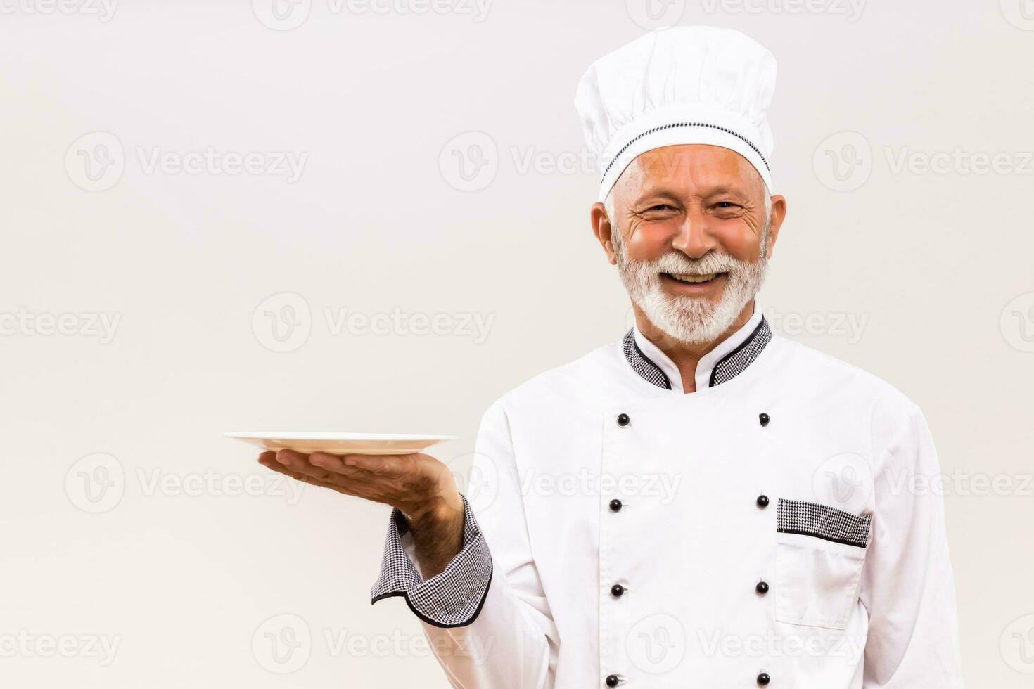 Portrait of senior chef with empty plate on gray background. photo