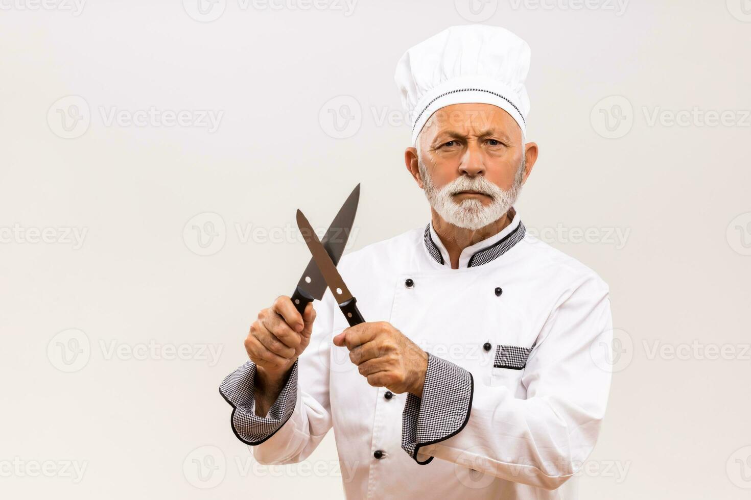 Image of angry chef sharpens knives on gray background. photo