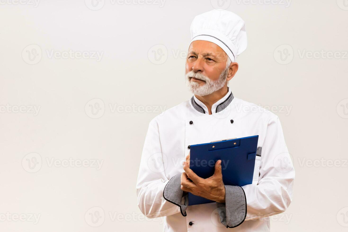 Portrait of senior  chef holding cookbook on gray background. photo