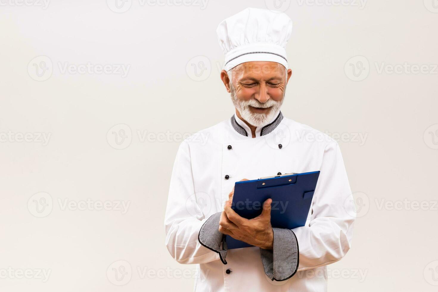 Portrait of senior  chef holding cookbook on gray background. photo