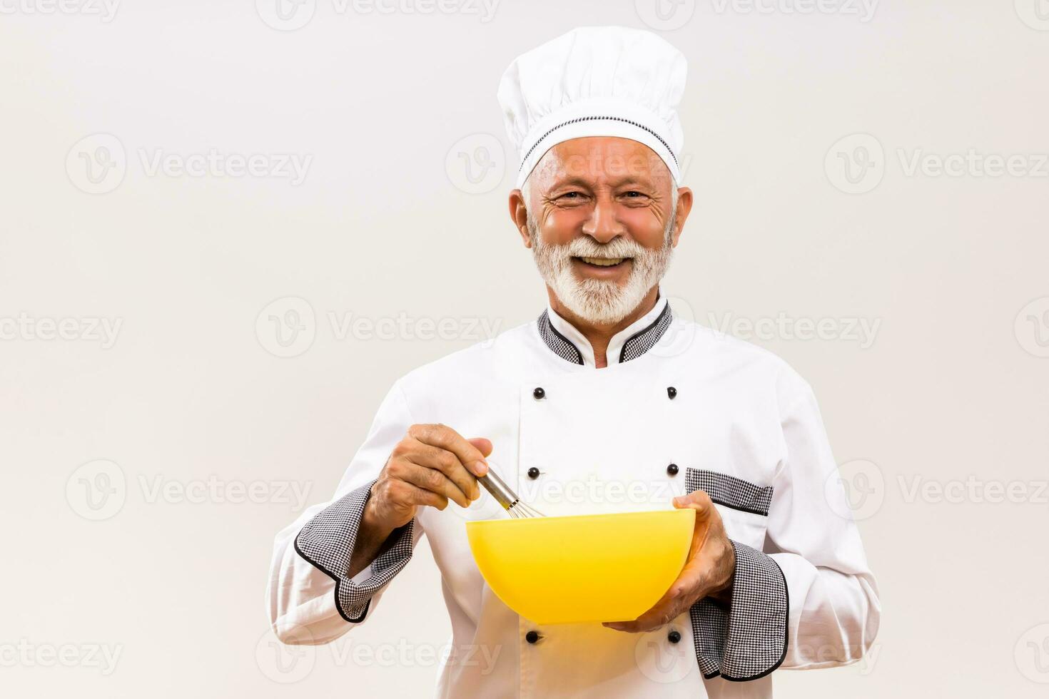 Senior chef holding bowl and wire whisk on gray background. photo
