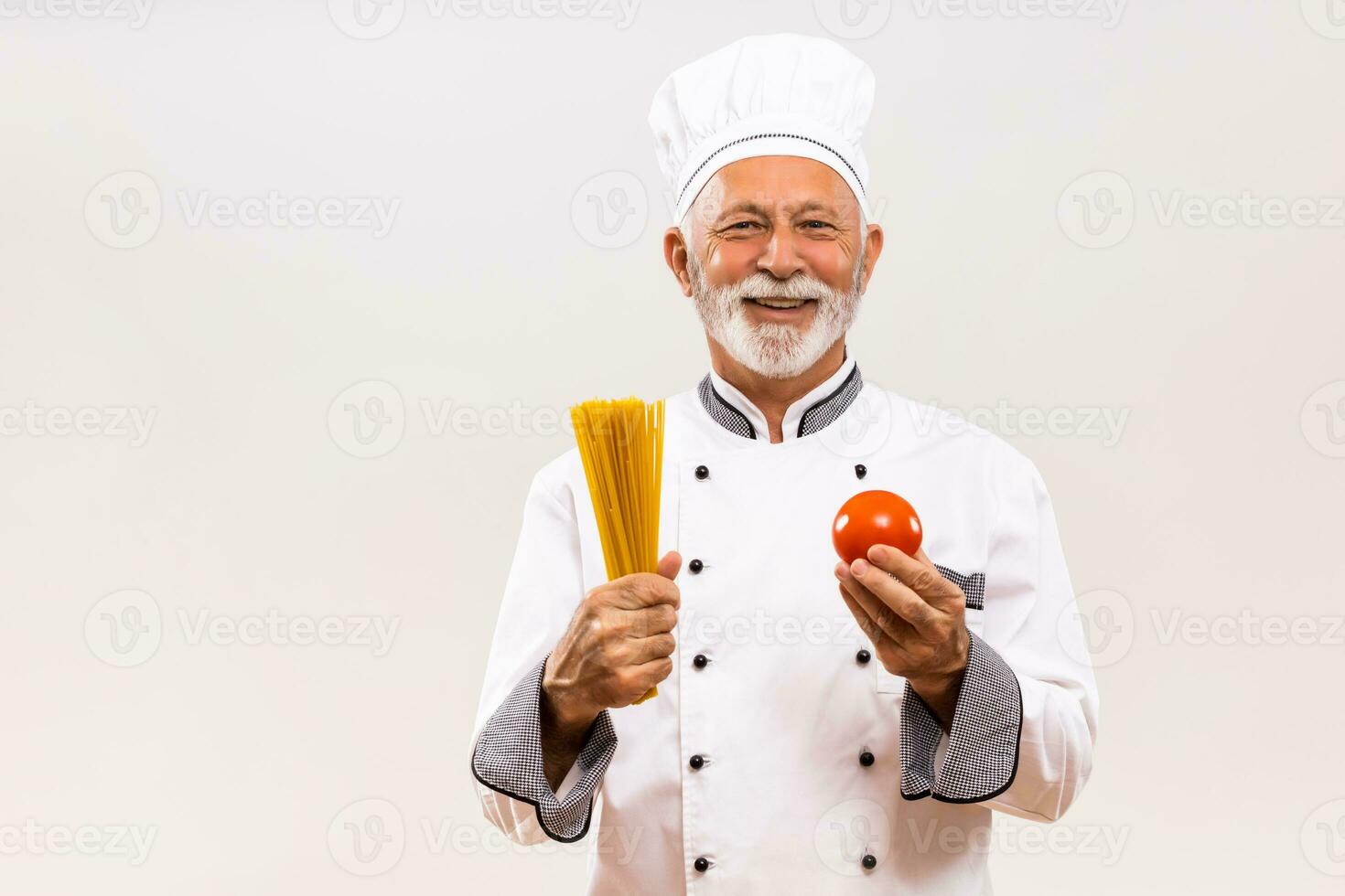 Portrait of senior chef holding tomato and spaghetti on gray background. photo