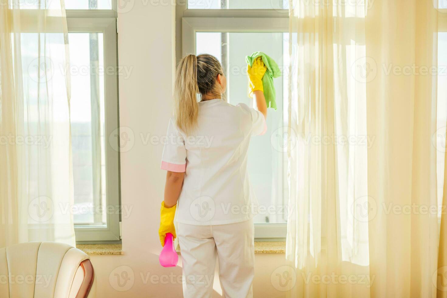 Image of hotel maid cleaning windows in a room. photo