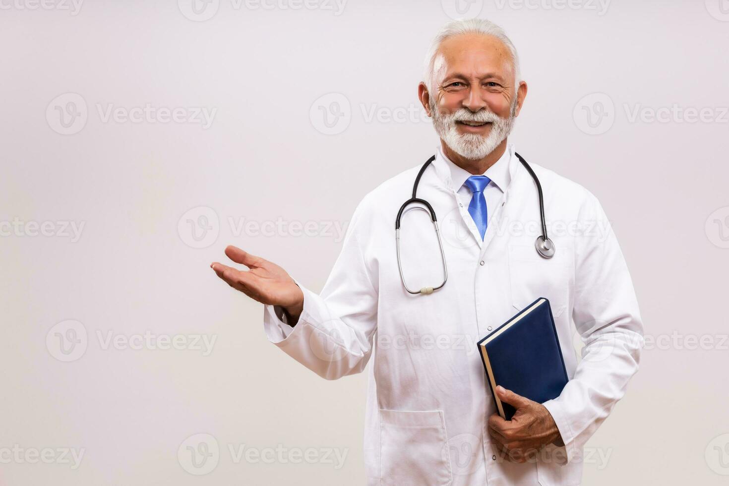 Portrait of senior doctor holding personal organizer and  showing welcome gesture on gray background. photo