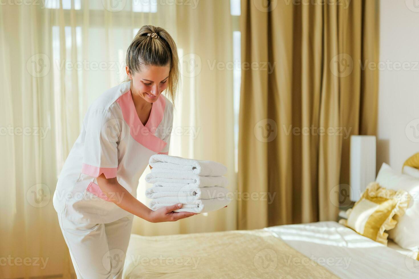 Beautiful hotel maid putting fresh and clean towels on bed in room photo