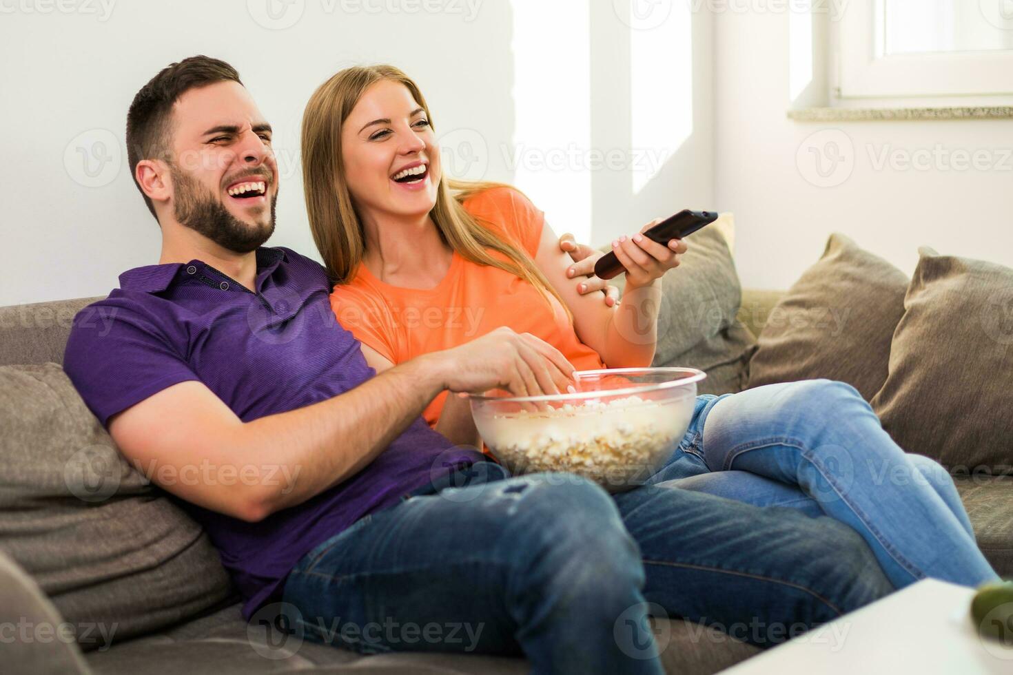Happy couple enjoy watching tv, eating popcorn and spending time together at their home. photo
