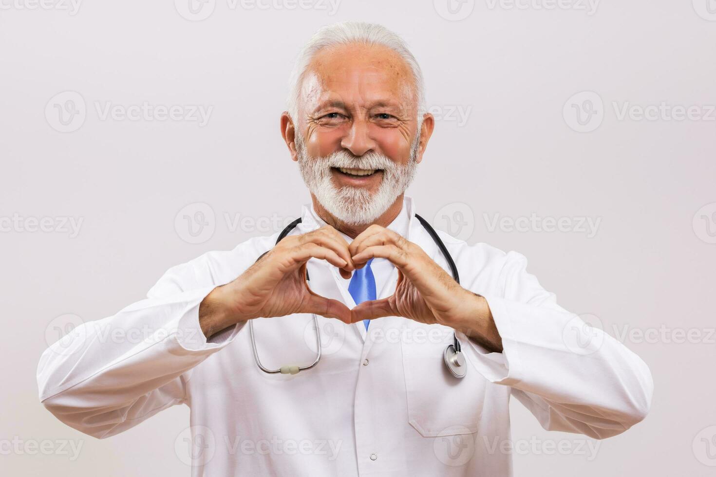 Portrait of senior doctor showing heart shape with hands on gray background. photo