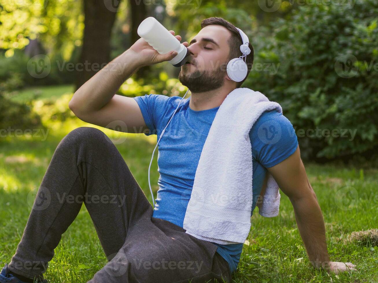 Handsome man with headphones  drinking water and resting after exercise in the park. photo