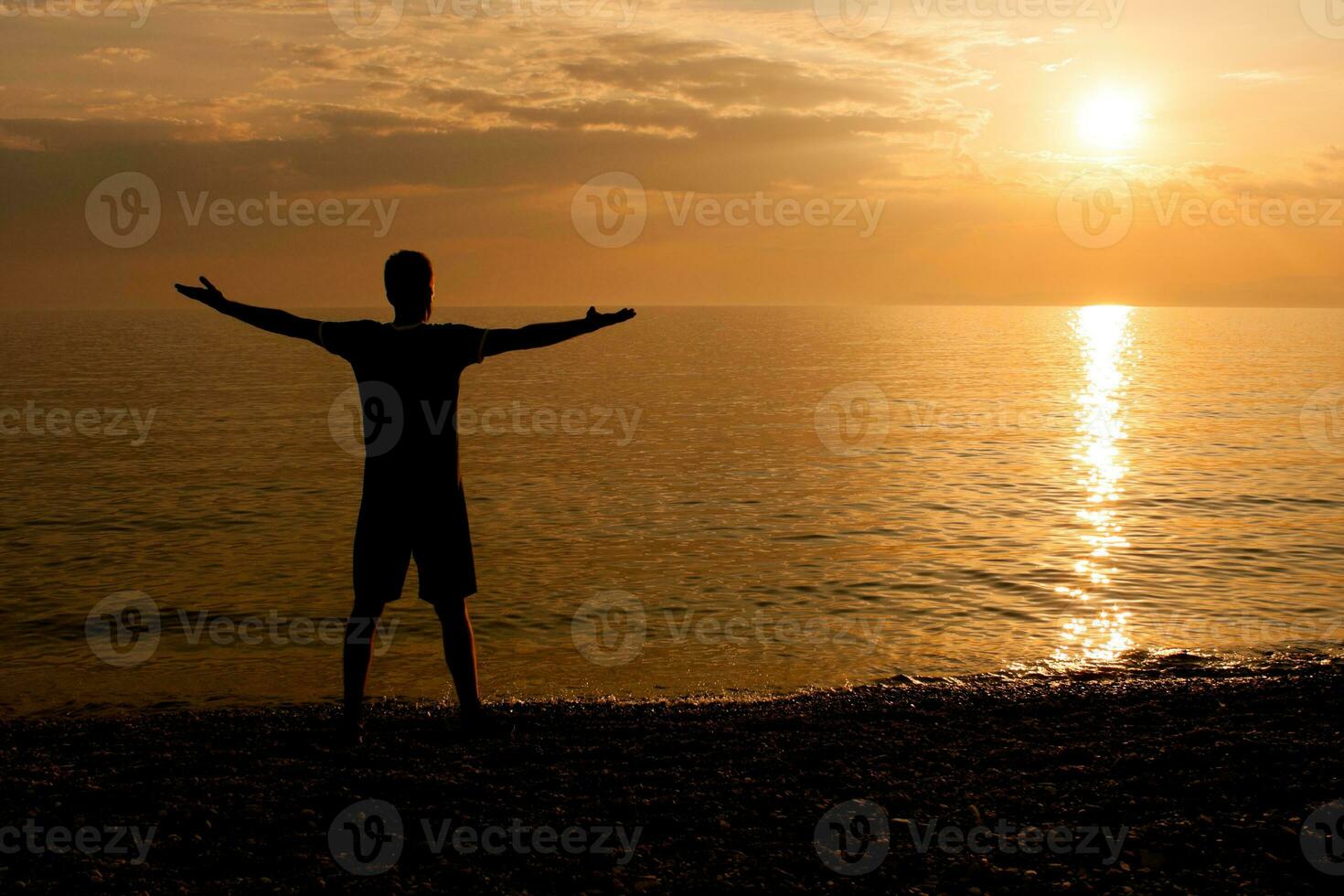 Silhouette of a man greeting the sunset at the sea photo