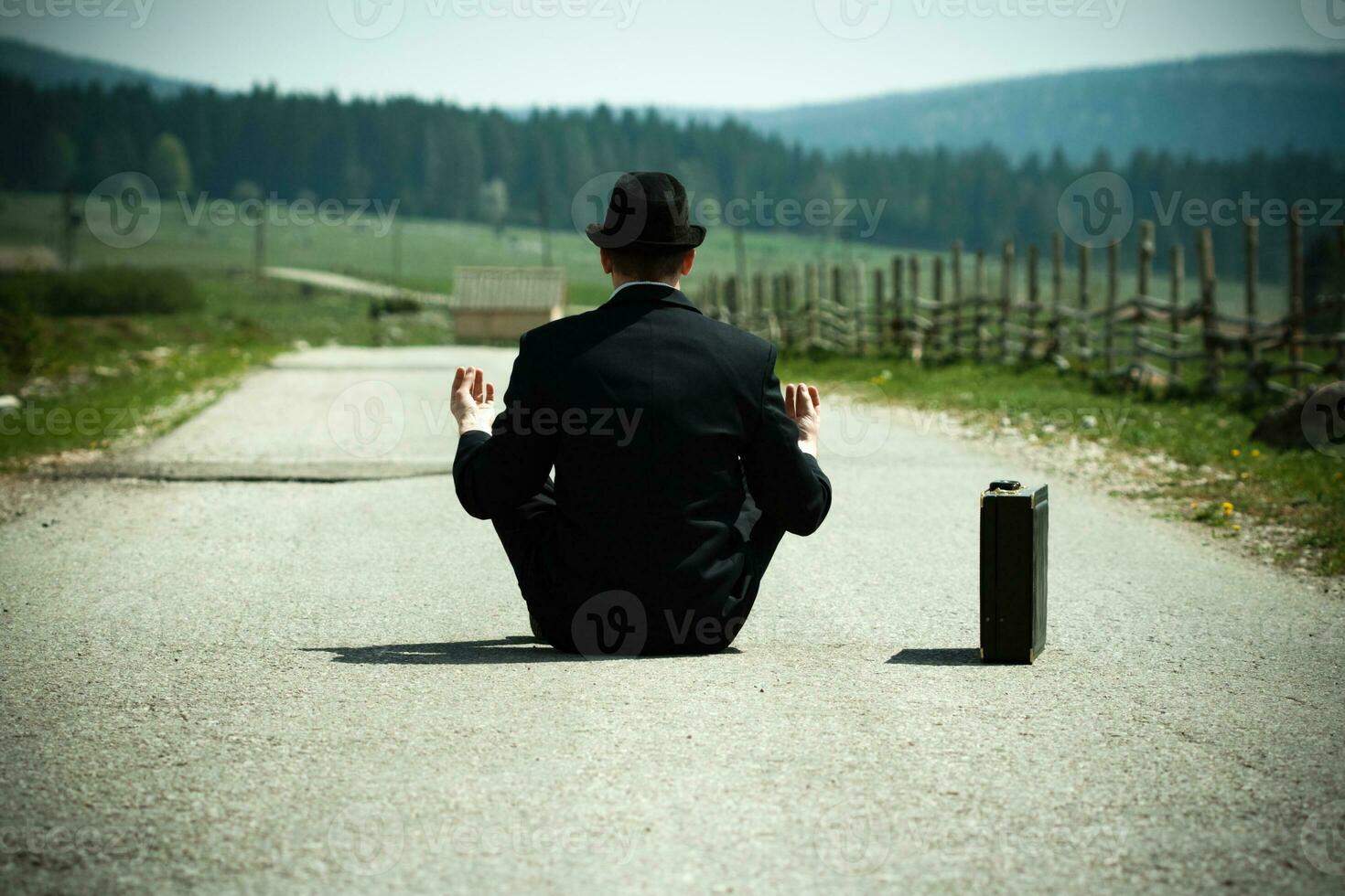 Ban in a suit sitting on the road with a suitcase and meditating photo