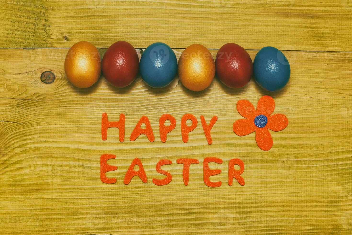 Happy Easter message with painted  eggs  and flower on wooden table.Toned photo. photo